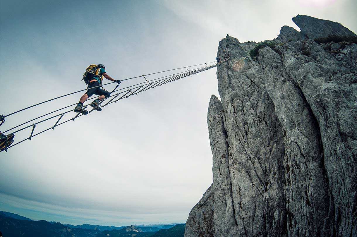 Hiker on steep roof ladder connected to the top of a rocky cliff
